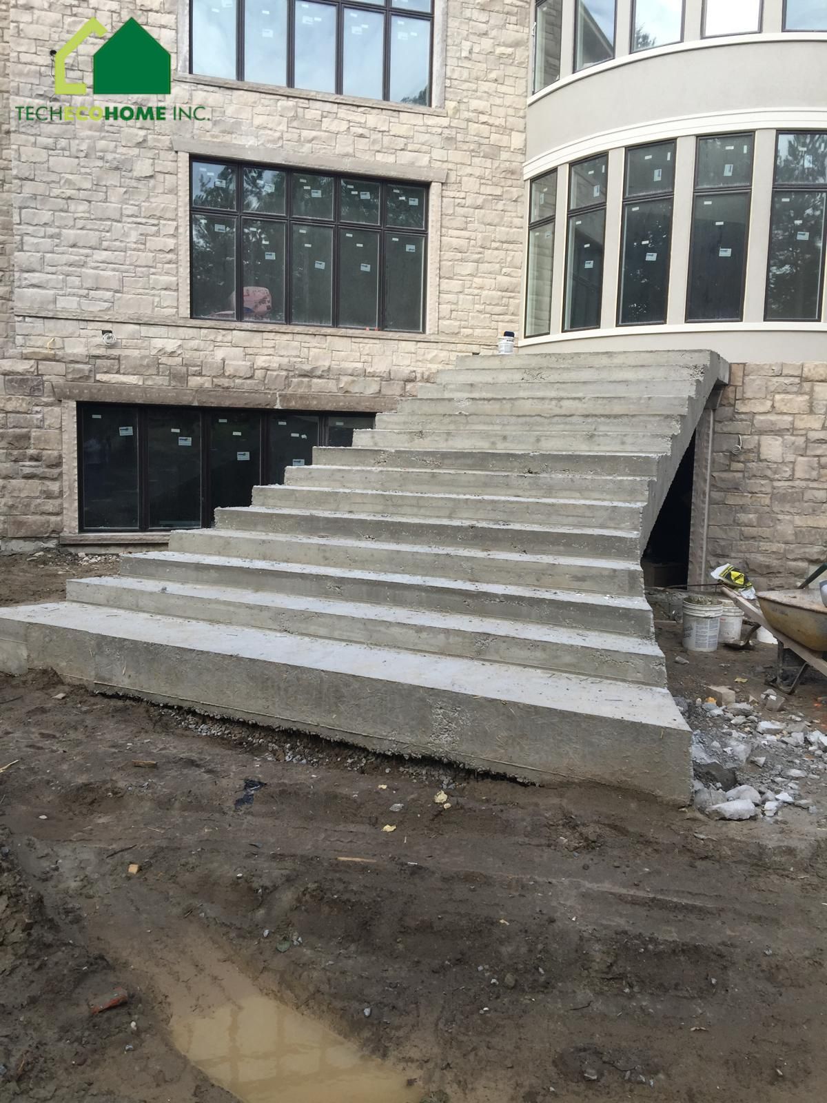Cast-in-place concrete entrance stairs at a stone-clad house with the TECHECOHOME INC. logo