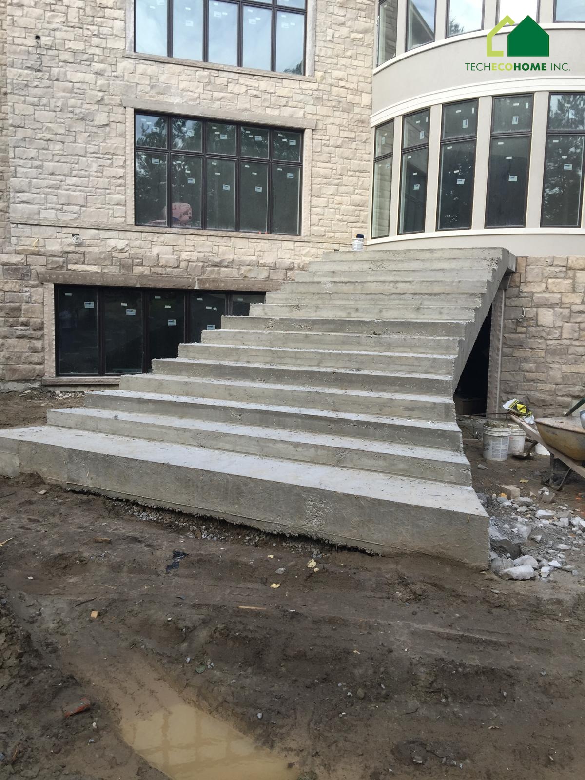 Wide cast-in-place concrete entrance stairs at a stone-clad house